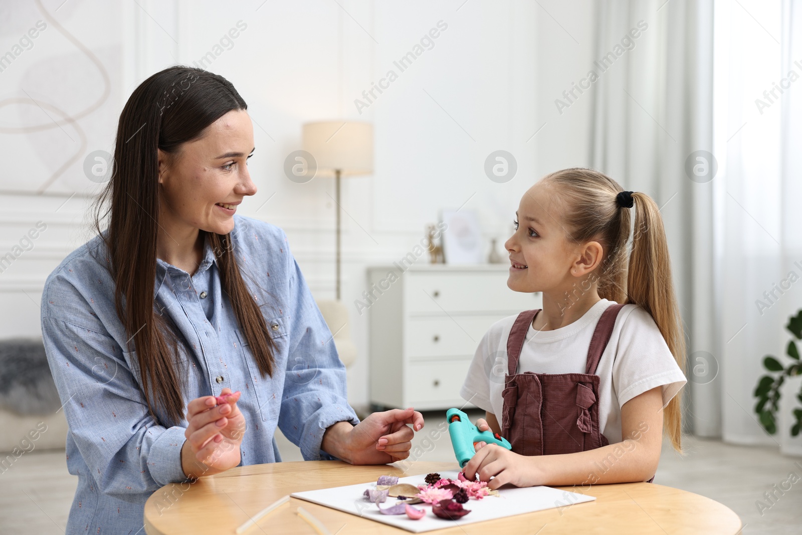 Photo of Mother and daughter with hot glue gun making craft at table indoors