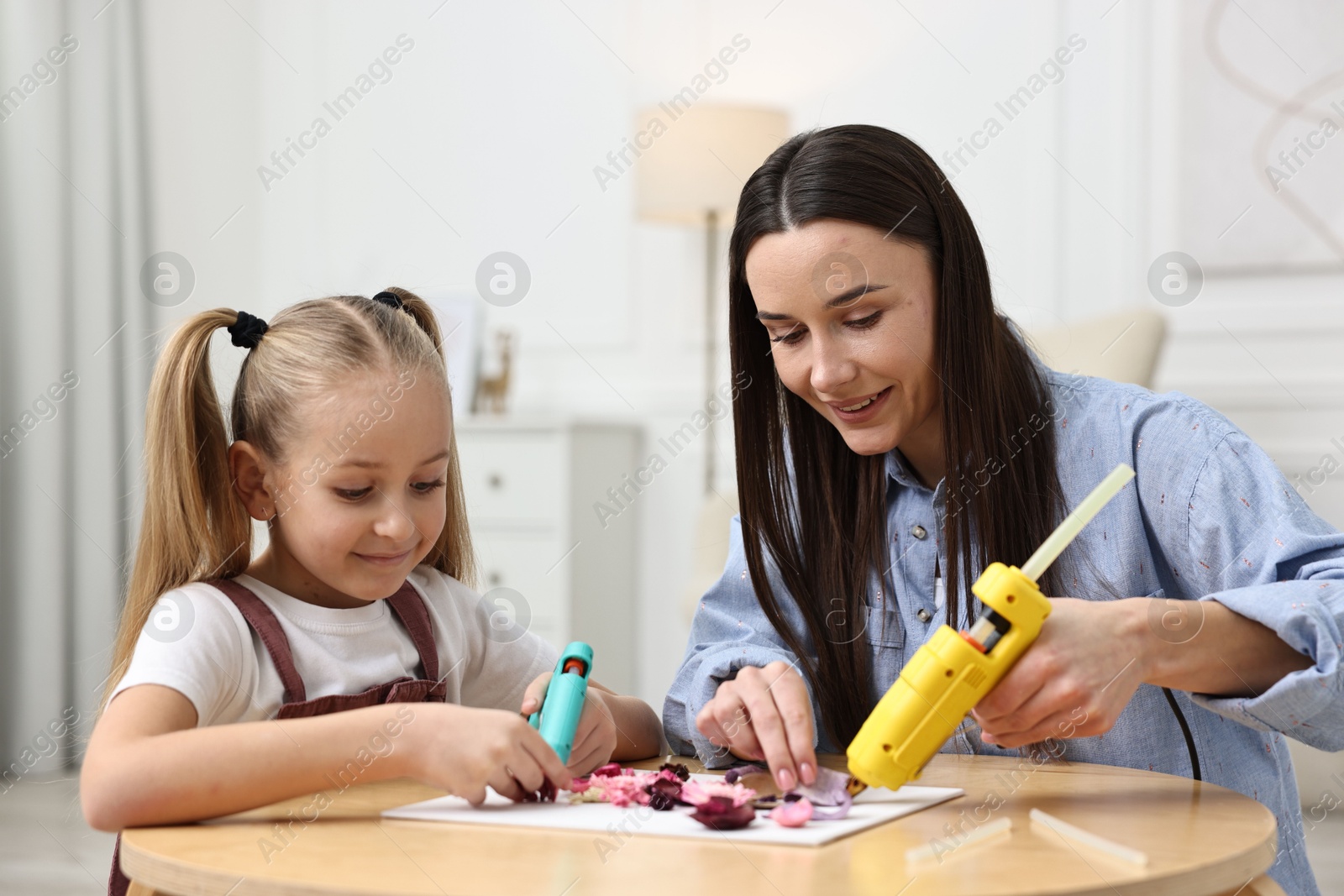 Photo of Mother and daughter with hot glue guns making craft at table indoors