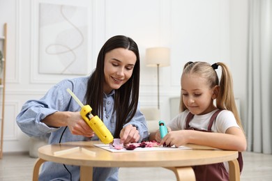 Photo of Mother and daughter with hot glue guns making craft at table indoors