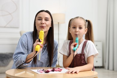 Photo of Family portrait of mother and daughter with hot glue guns at table indoors