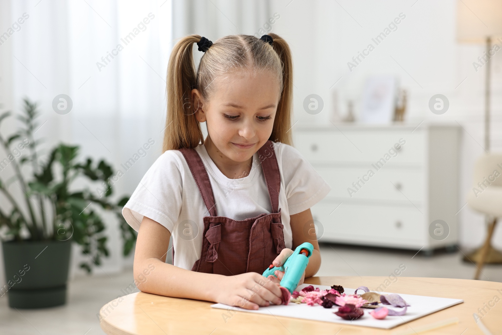 Photo of Little girl with hot glue gun making craft at table indoors