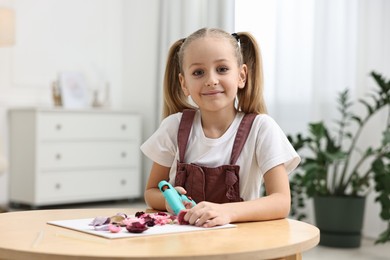 Photo of Little girl with hot glue gun making craft at table indoors