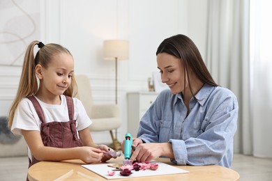 Photo of Mother and daughter with hot glue gun making craft at table indoors