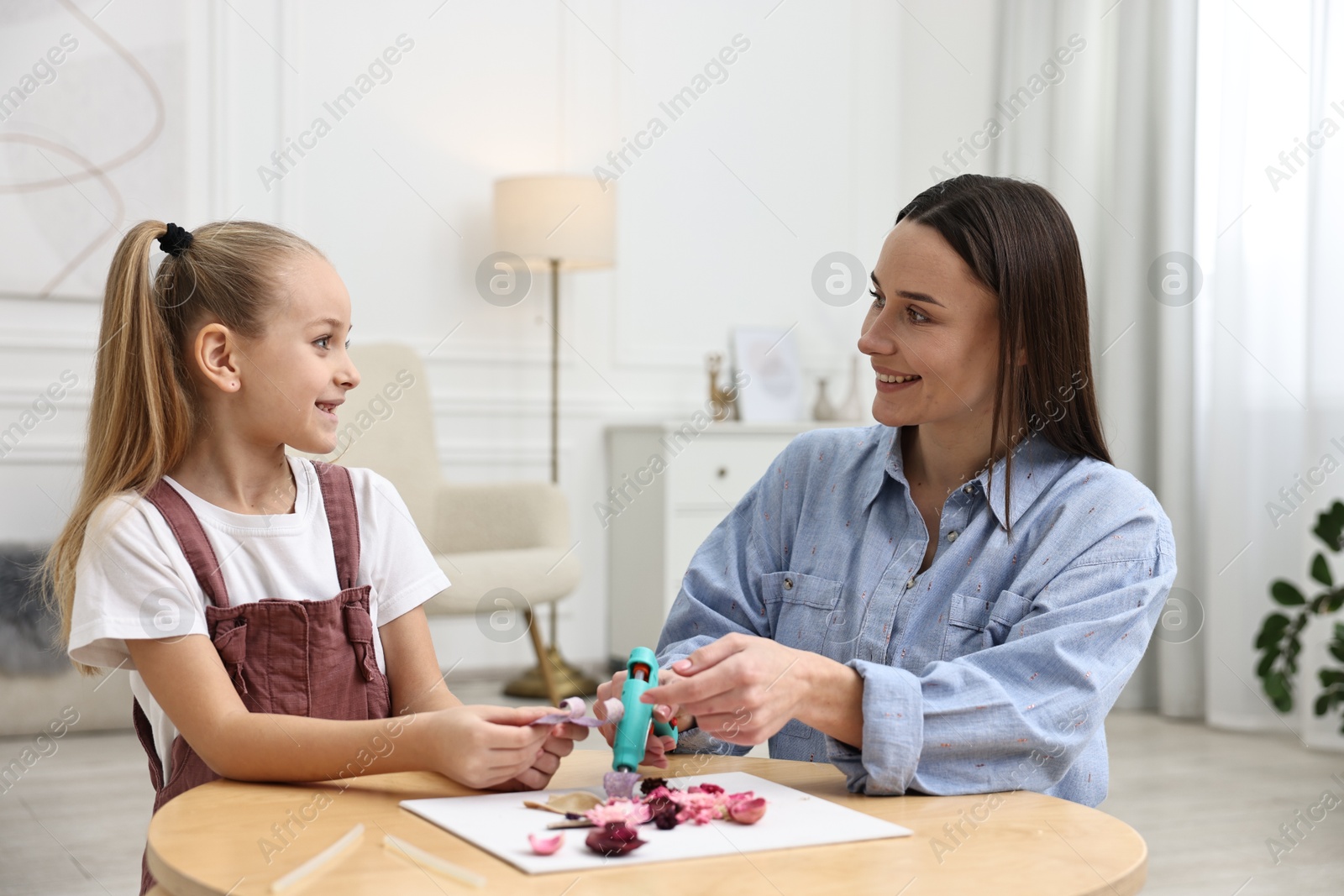 Photo of Mother and daughter with hot glue gun making craft at table indoors