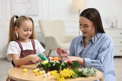 Photo of Mother and daughter with hot glue gun creating Easter composition at table indoors