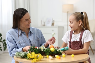 Photo of Mother and daughter with hot glue gun creating Easter composition at table indoors