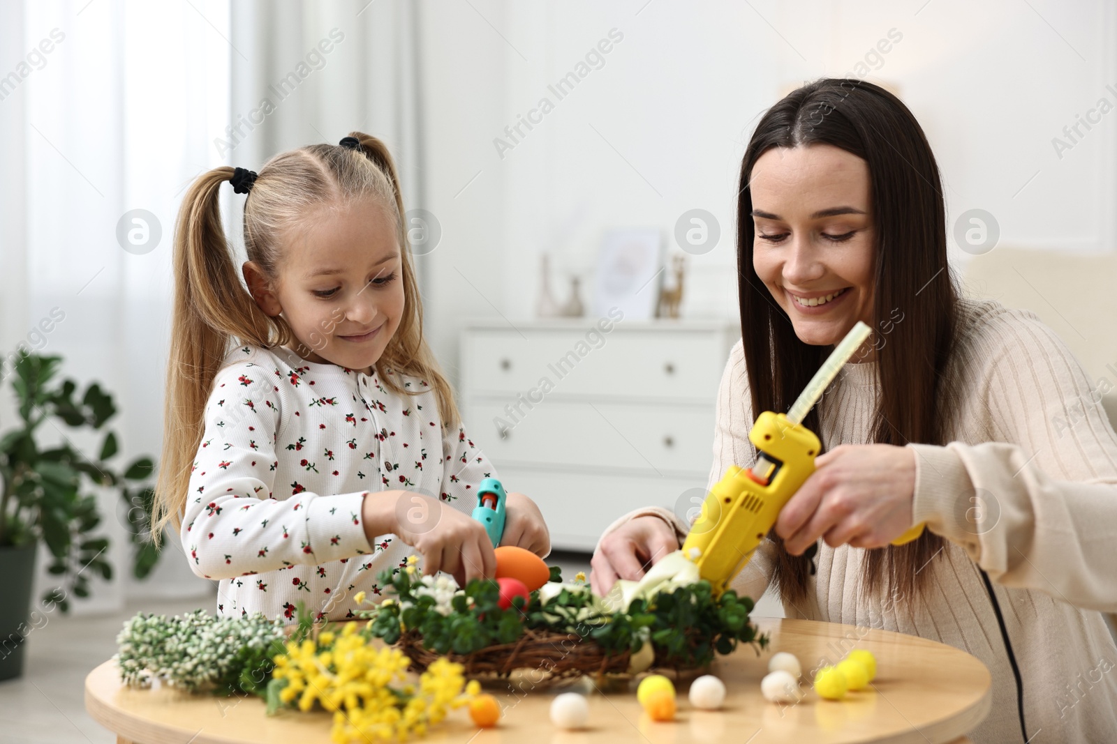 Photo of Mother and daughter with hot glue guns creating Easter composition at table indoors