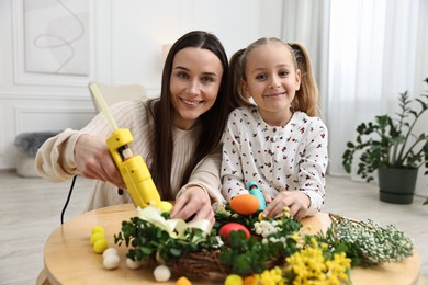 Photo of Mother and daughter with hot glue guns creating Easter composition at table indoors