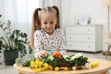 Photo of Little girl with hot glue gun creating Easter composition at table indoors