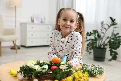 Photo of Little girl with hot glue gun creating Easter composition at table indoors