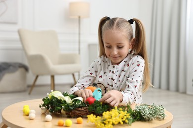 Photo of Little girl with hot glue gun creating Easter composition at table indoors