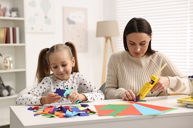 Photo of Mother and daughter with hot glue guns and color paper making craft at table indoors