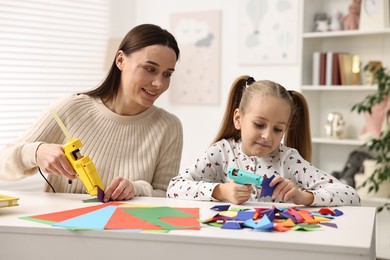 Photo of Mother and daughter with hot glue guns and color paper making craft at table indoors