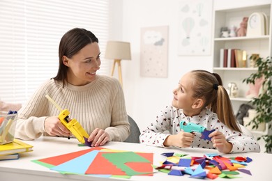 Mother and daughter with hot glue guns and color paper making craft at table indoors