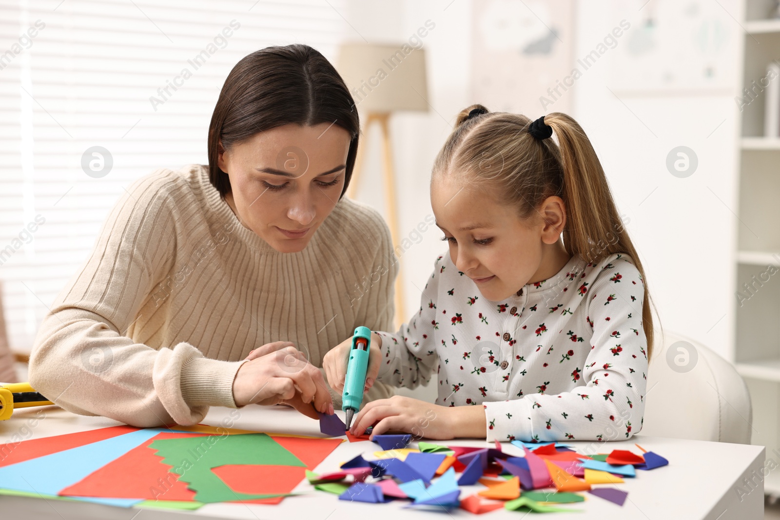 Photo of Mother and daughter with hot glue gun and color paper making craft at table indoors