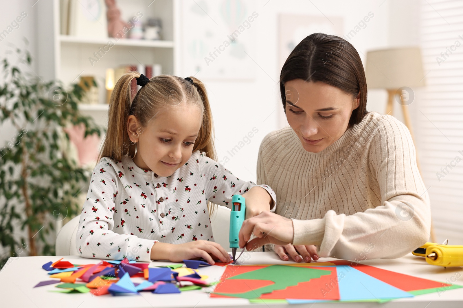 Photo of Mother and daughter with hot glue gun and color paper making craft at table indoors