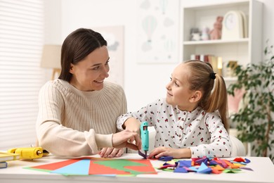 Photo of Mother and daughter with hot glue gun and color paper making craft at table indoors