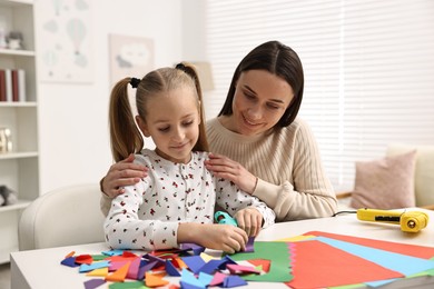 Photo of Mother and daughter with hot glue gun and color paper making craft at table indoors