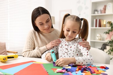 Photo of Mother and daughter with hot glue gun and color paper making craft at table indoors