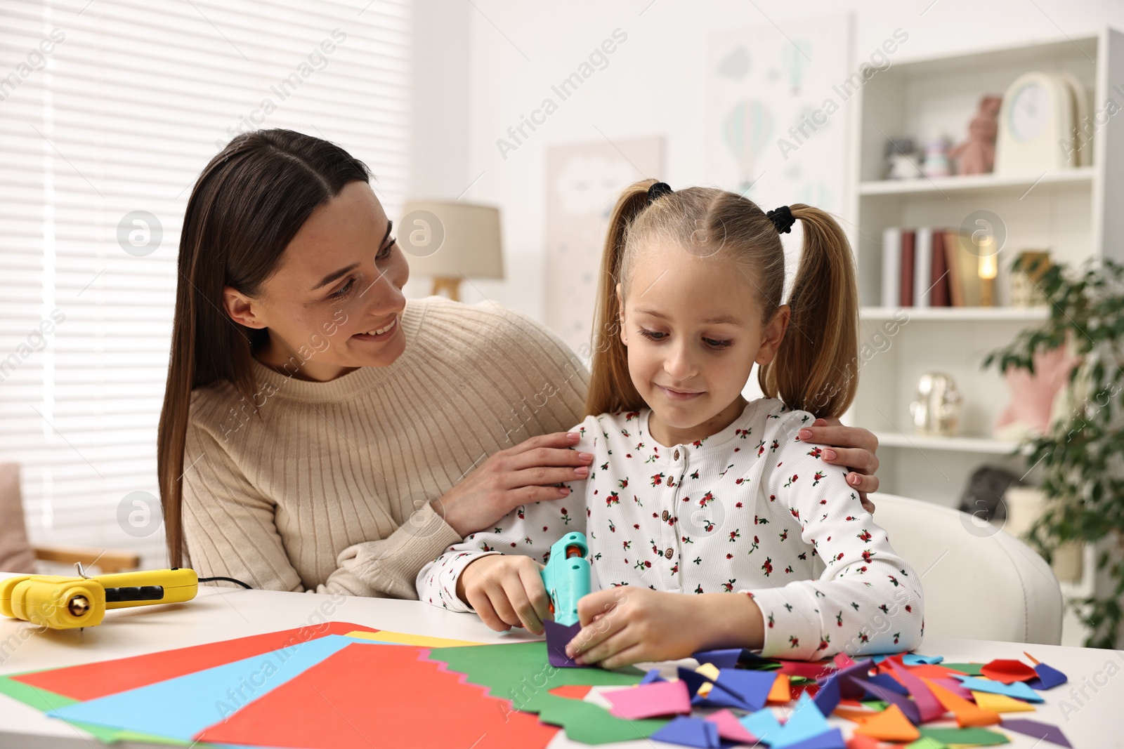 Photo of Mother and daughter with hot glue gun and color paper making craft at table indoors