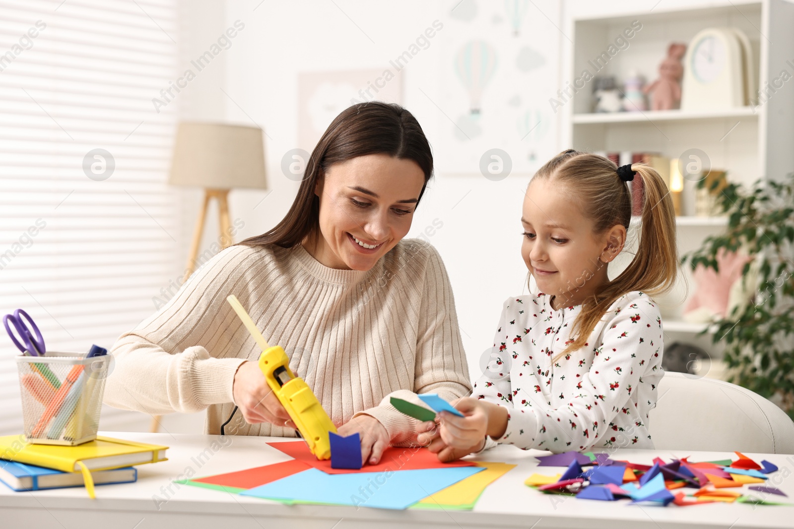 Photo of Mother and daughter with hot glue gun and color paper making craft at table indoors