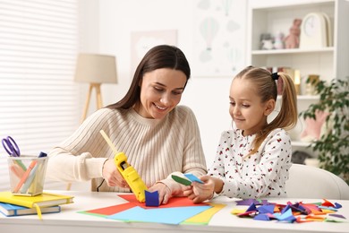 Photo of Mother and daughter with hot glue gun and color paper making craft at table indoors