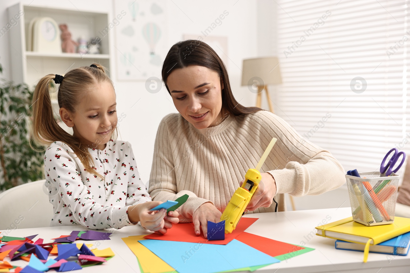 Photo of Mother and daughter with hot glue gun and color paper making craft at table indoors