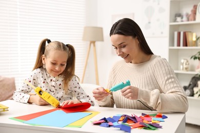 Photo of Mother and daughter with hot glue guns and color paper making craft at table indoors