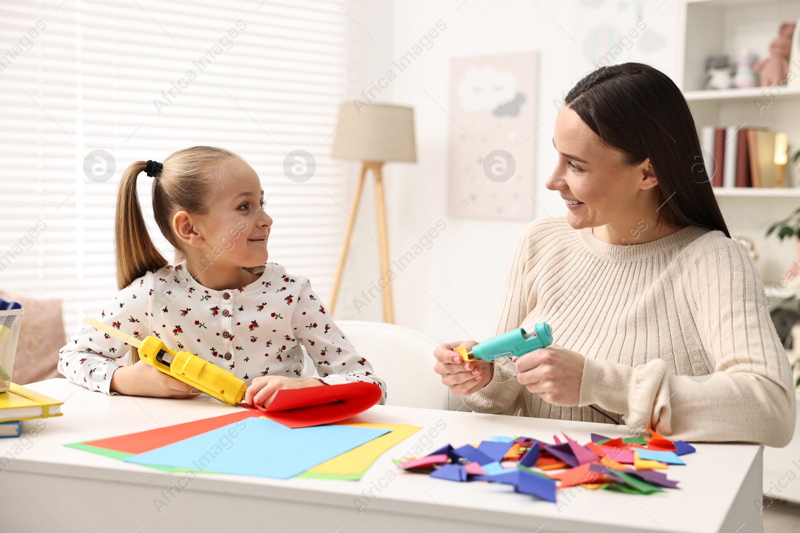 Photo of Mother and daughter with hot glue guns and color paper making craft at table indoors