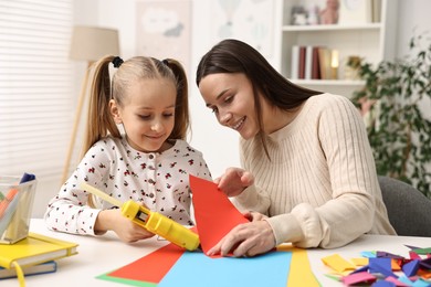 Photo of Mother and daughter with hot glue gun and color paper making craft at table indoors