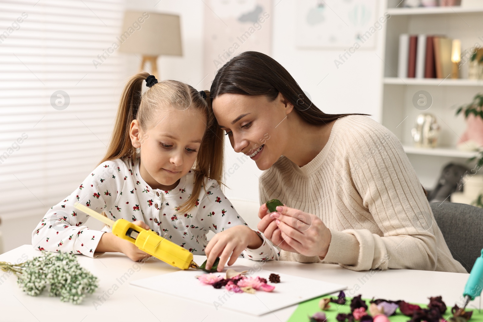 Photo of Mother and daughter with hot glue gun making craft at table indoors