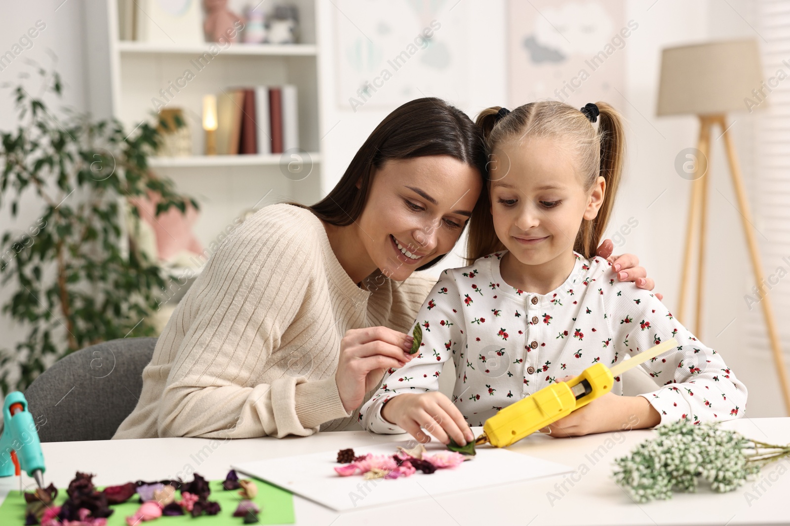 Photo of Mother and daughter with hot glue gun making craft at table indoors