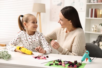 Photo of Mother and daughter with hot glue gun making craft at table indoors