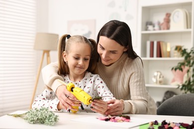 Photo of Mother and daughter with hot glue gun making craft at table indoors