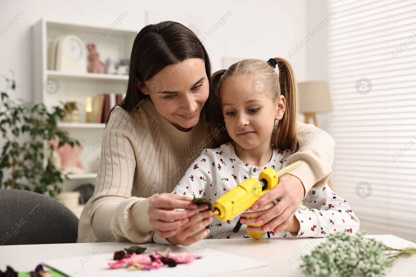 Photo of Mother and daughter with hot glue gun making craft at table indoors