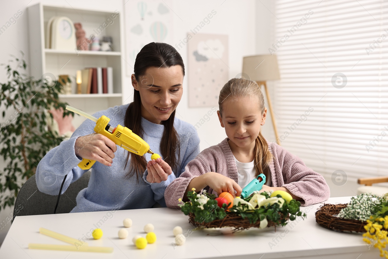 Photo of Mother and daughter with hot glue guns creating Easter composition at table indoors