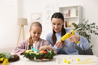 Photo of Mother and daughter with hot glue guns creating Easter composition at table indoors