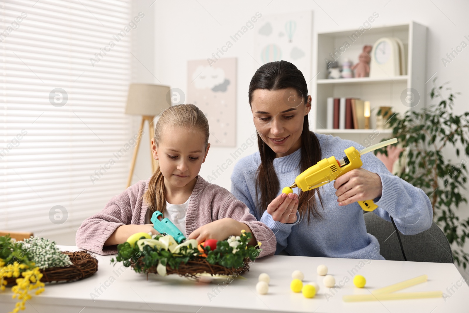 Photo of Mother and daughter with hot glue guns creating Easter composition at table indoors