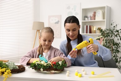 Photo of Mother and daughter with hot glue guns creating Easter composition at table indoors