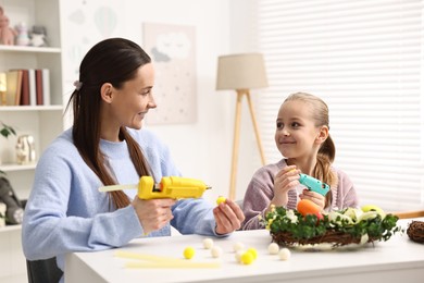 Photo of Mother and daughter with hot glue guns creating Easter composition at table indoors