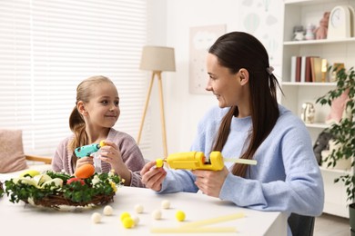 Photo of Mother and daughter with hot glue guns creating Easter composition at table indoors