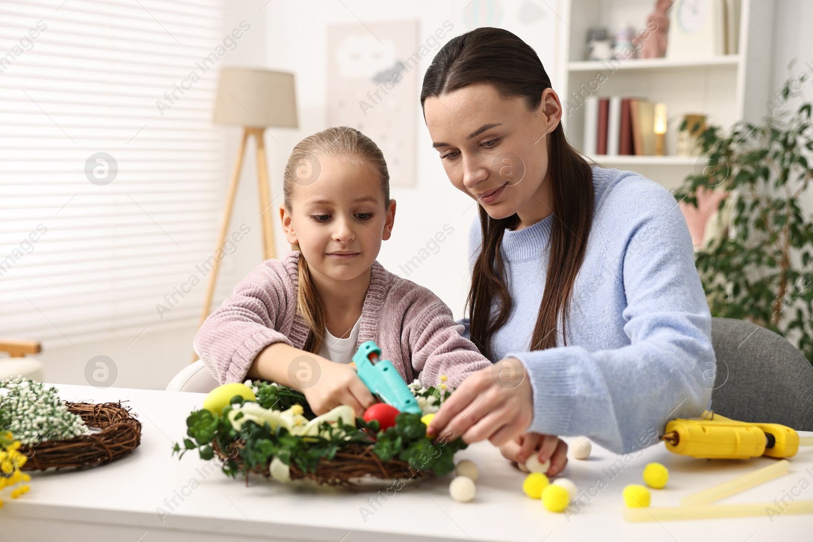 Photo of Mother and daughter with hot glue guns creating Easter composition at table indoors