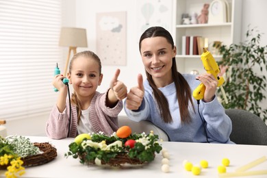 Photo of Mother and daughter with hot glue guns showing thumbs up at table indoors