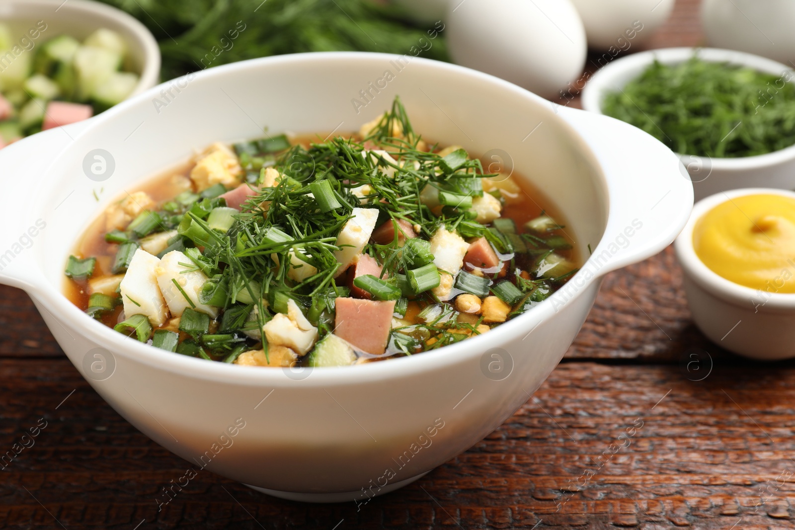 Photo of Delicious okroshka soup and ingredients on wooden table, closeup