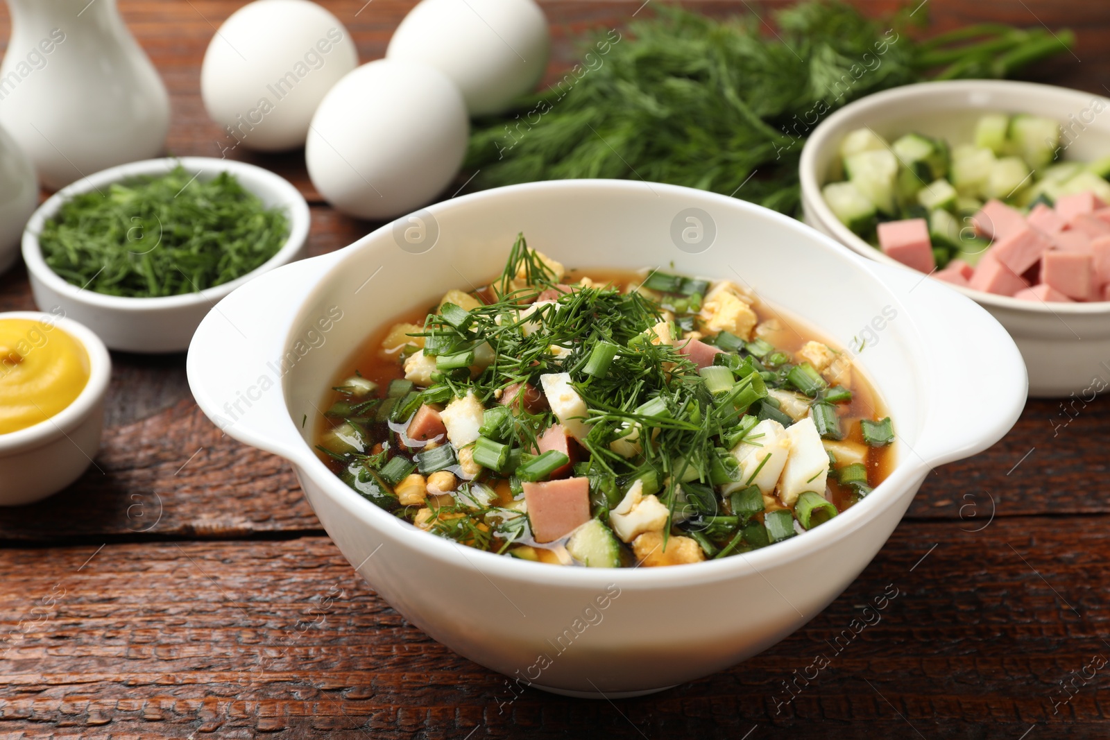 Photo of Delicious okroshka soup and ingredients on wooden table, closeup