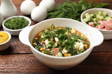 Photo of Delicious okroshka soup and ingredients on wooden table, closeup