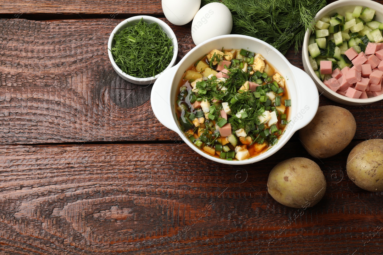 Photo of Delicious okroshka soup and ingredients on wooden table, flat lay. Space for text