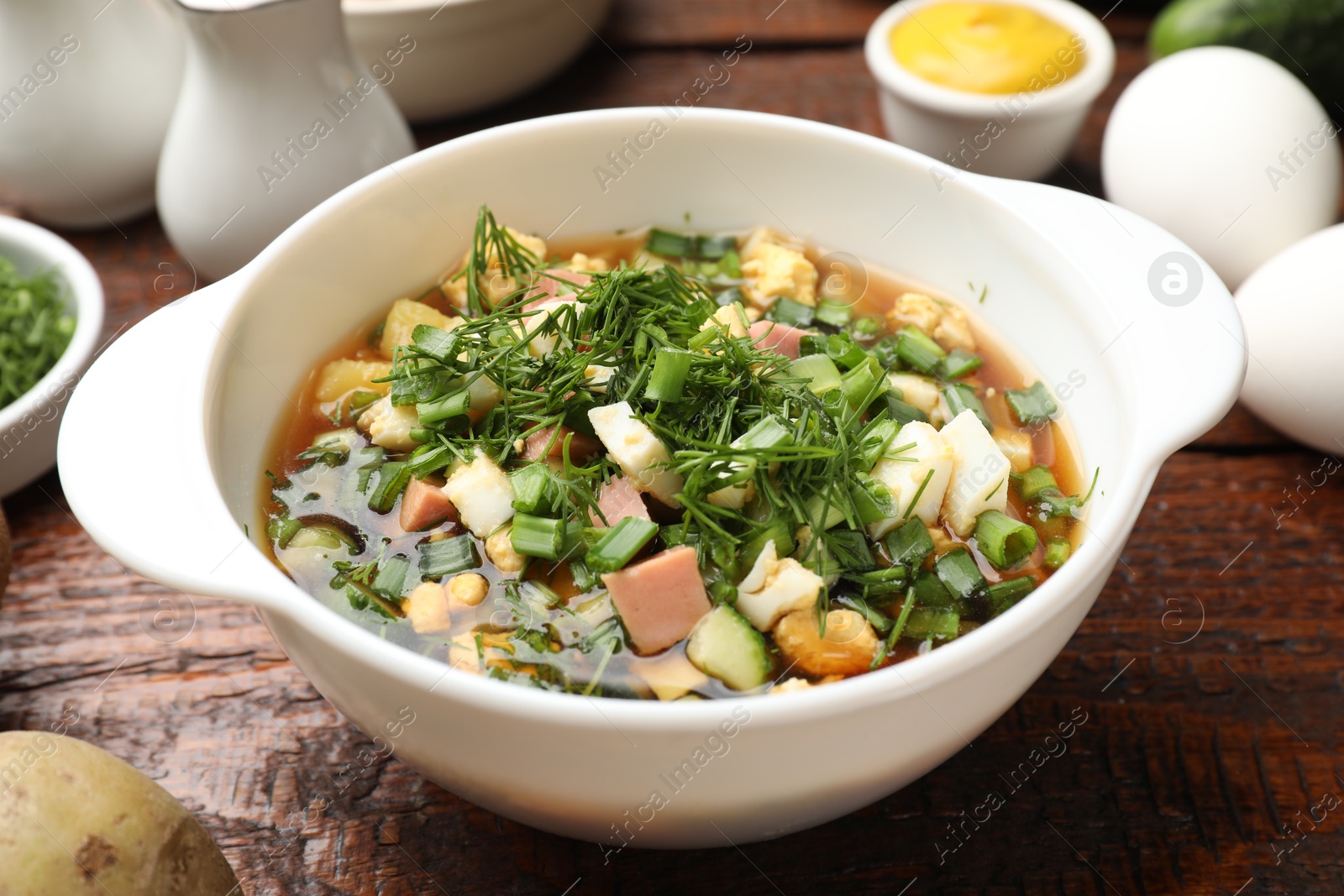 Photo of Delicious okroshka soup and ingredients on wooden table, closeup