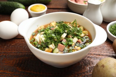 Photo of Delicious okroshka soup and ingredients on wooden table, closeup