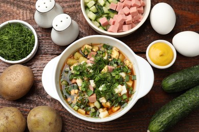 Photo of Delicious okroshka soup and ingredients on wooden table, flat lay